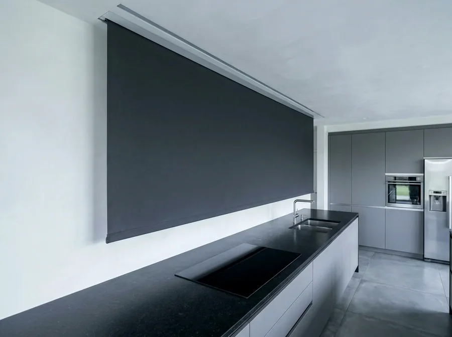 Concealed blind dropping from a recessed ceiling slot above a kitchen wall